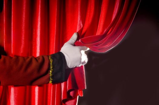 Una mano con guante blanco corre la cortina de un escenario